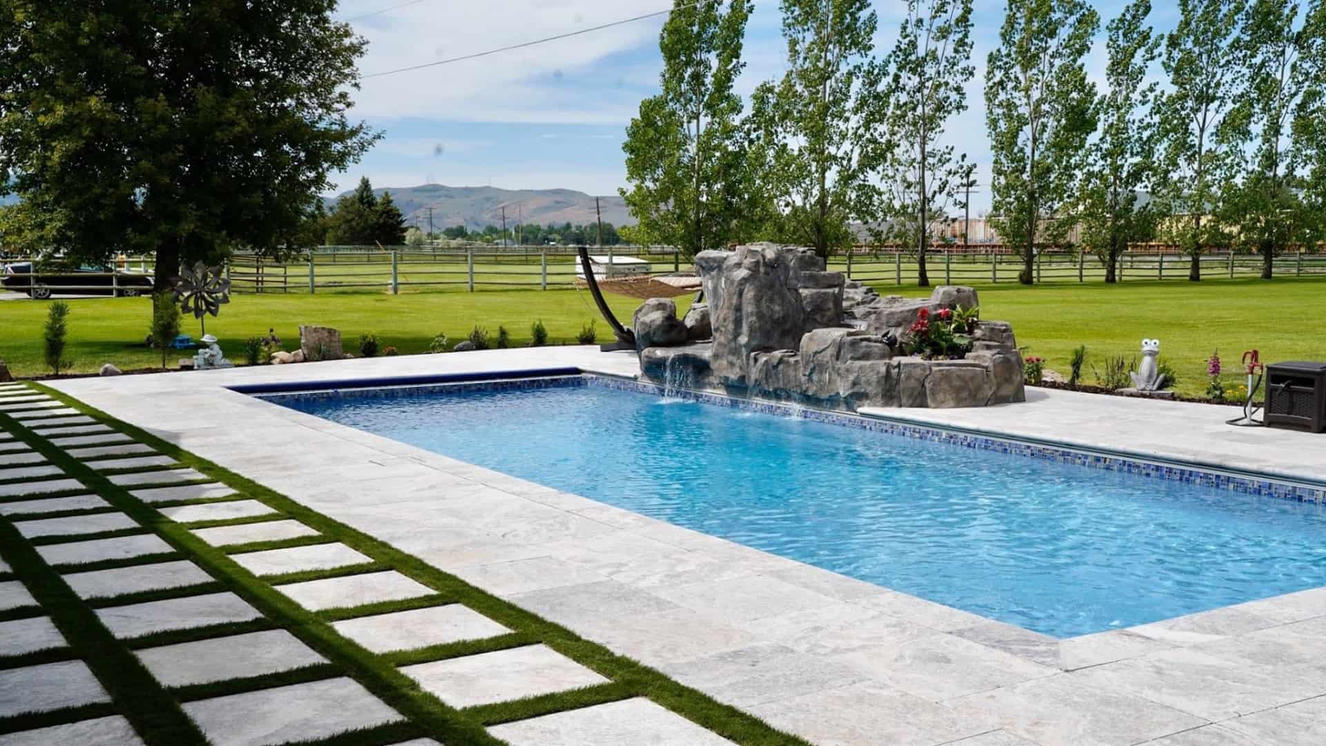 A backyard pool with grass and trees behind