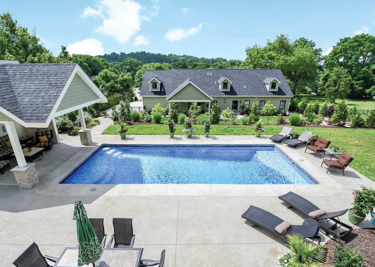 An arial view shows a pristine, rectangular in-ground pool in the backyard of a lovely home. Regular pool maintenance keeps the pool in pristine condition.