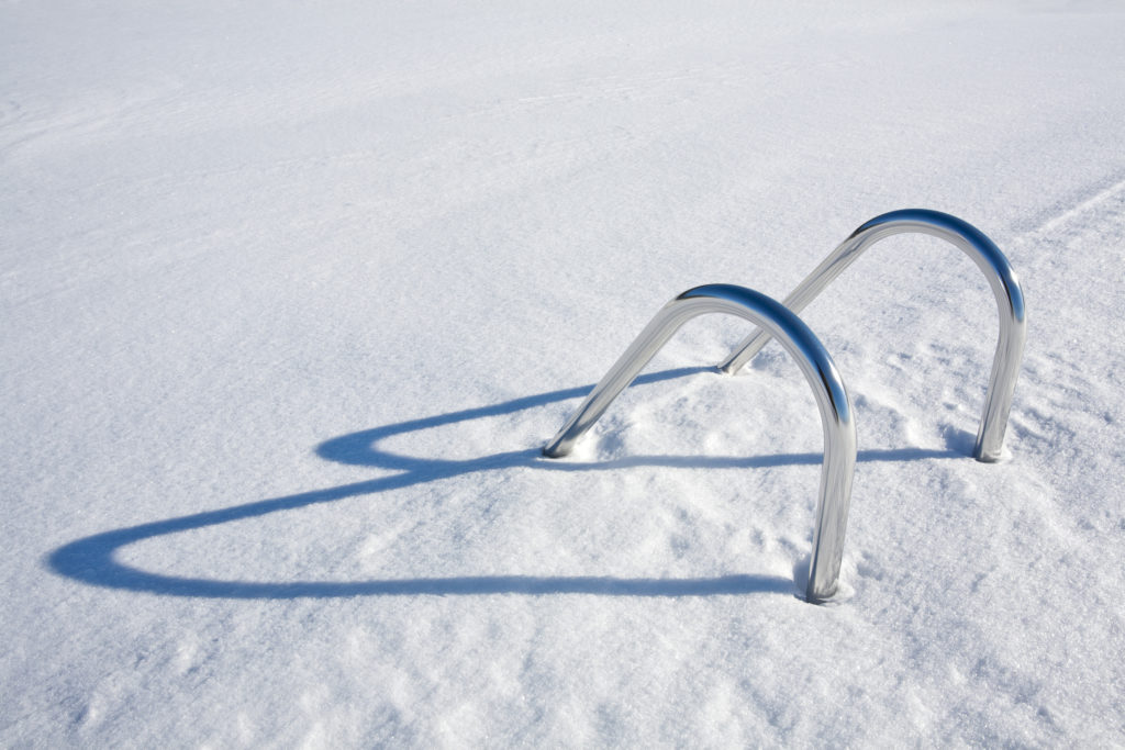 The handle bars to a swimming pool ladder stick out of thick snow. 
