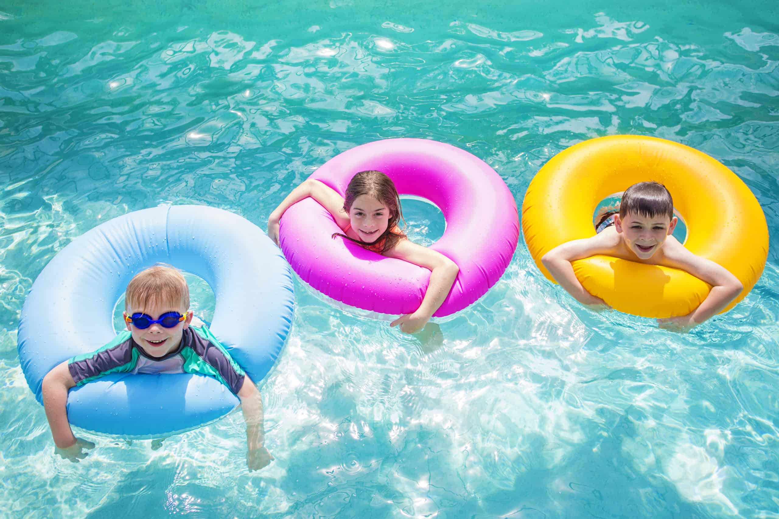Three young swimmers float in multi-colored inner tubes and smile as they practice swim safety tips.