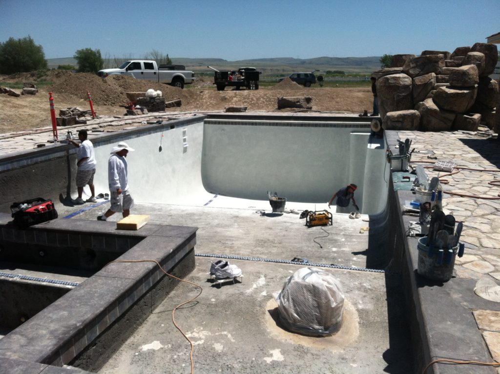 A swimming pool building crew uses shotcrete to build an inground pool. The difference between shotcrete and gunite is simple application.