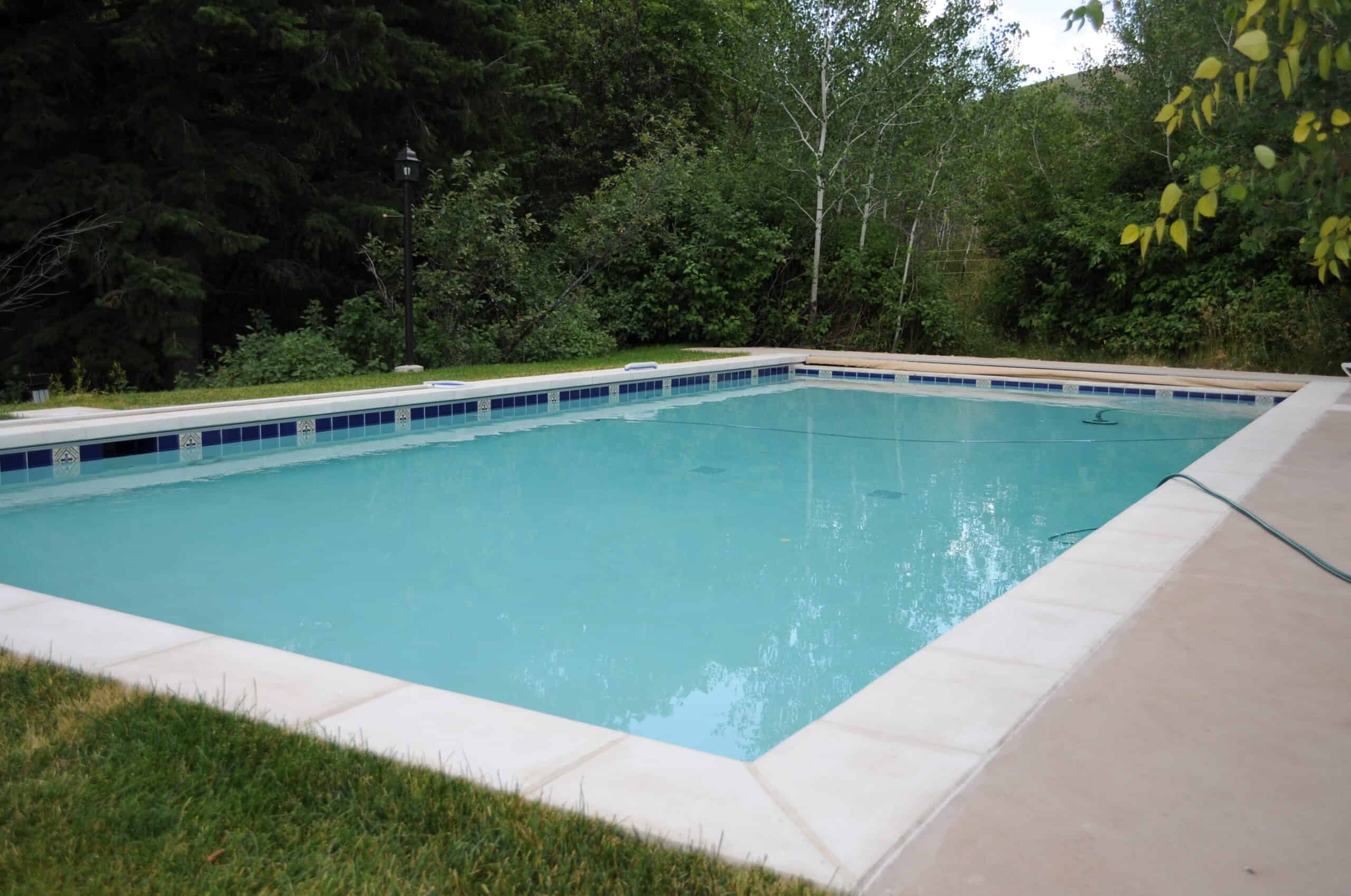 An in ground swimming pool sits nestled in lush, green woods awaiting its pool cover to be installed before it snows.