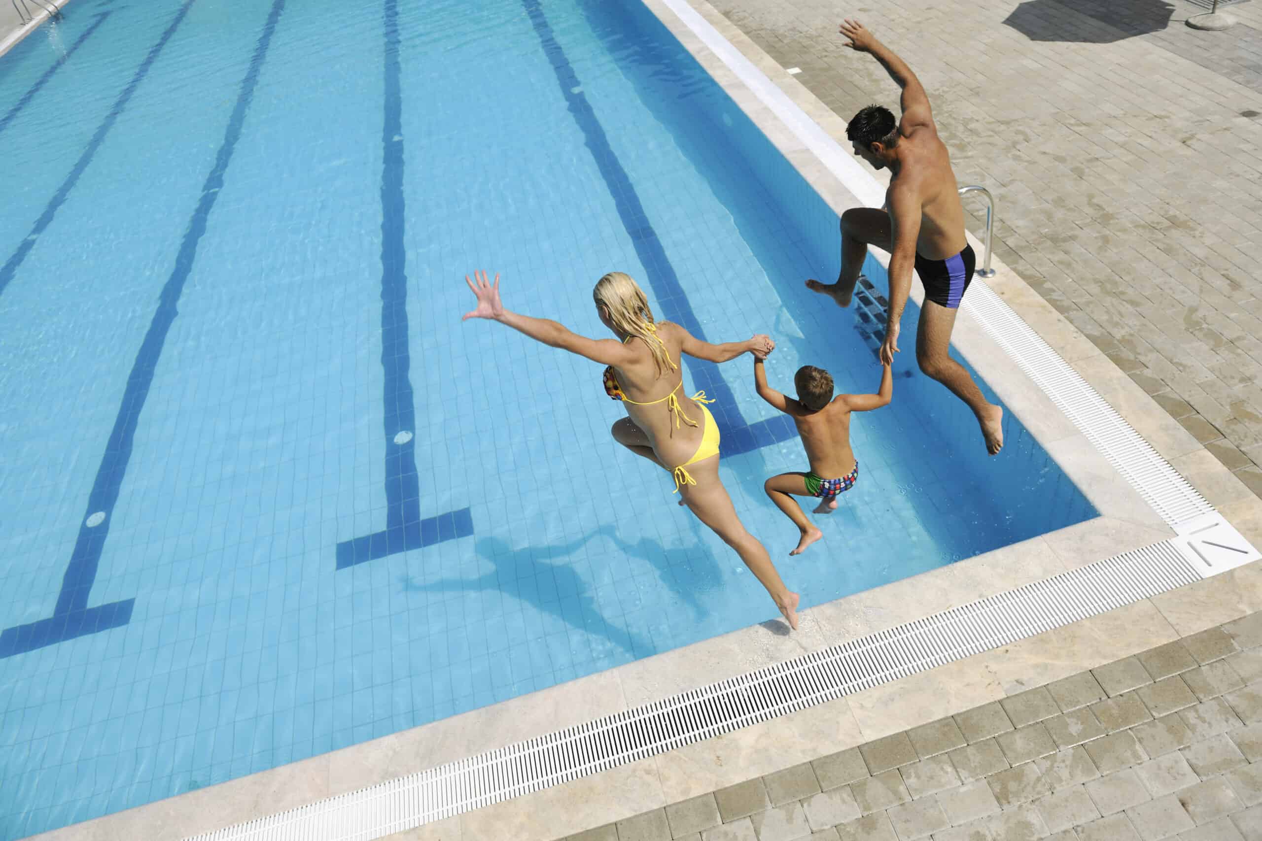 Pictured is a family of three mid air, jumping into a commercial pool. Commercial pool maintenance keeps pool clean.