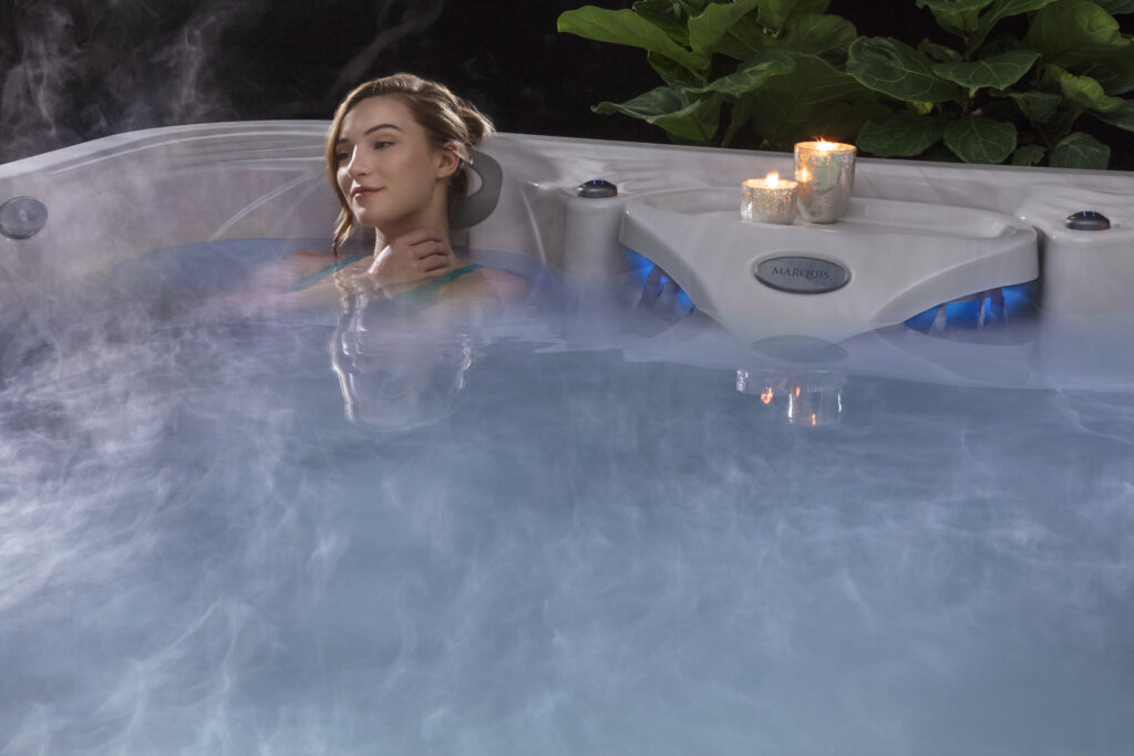A woman relaxing in a marquis hot tub. There are two candles along the edge of the tub.