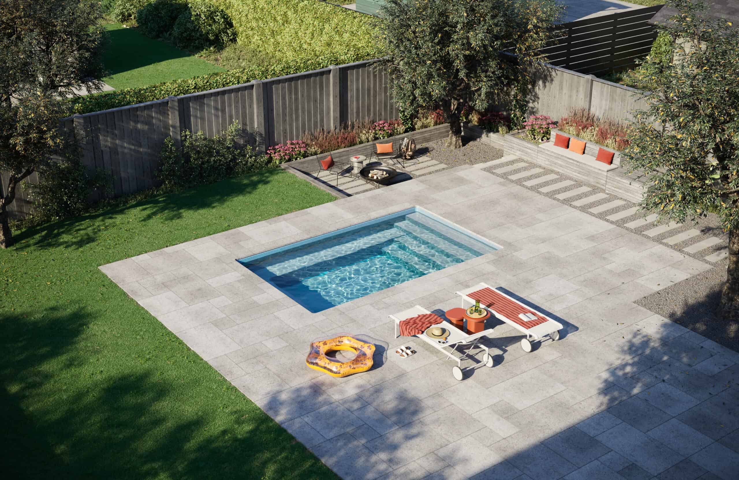 A rectangular swimming pool can be seen in a backyard. There is a stone patio surrounding the pool with some lounge chairs, towels, and pool float.