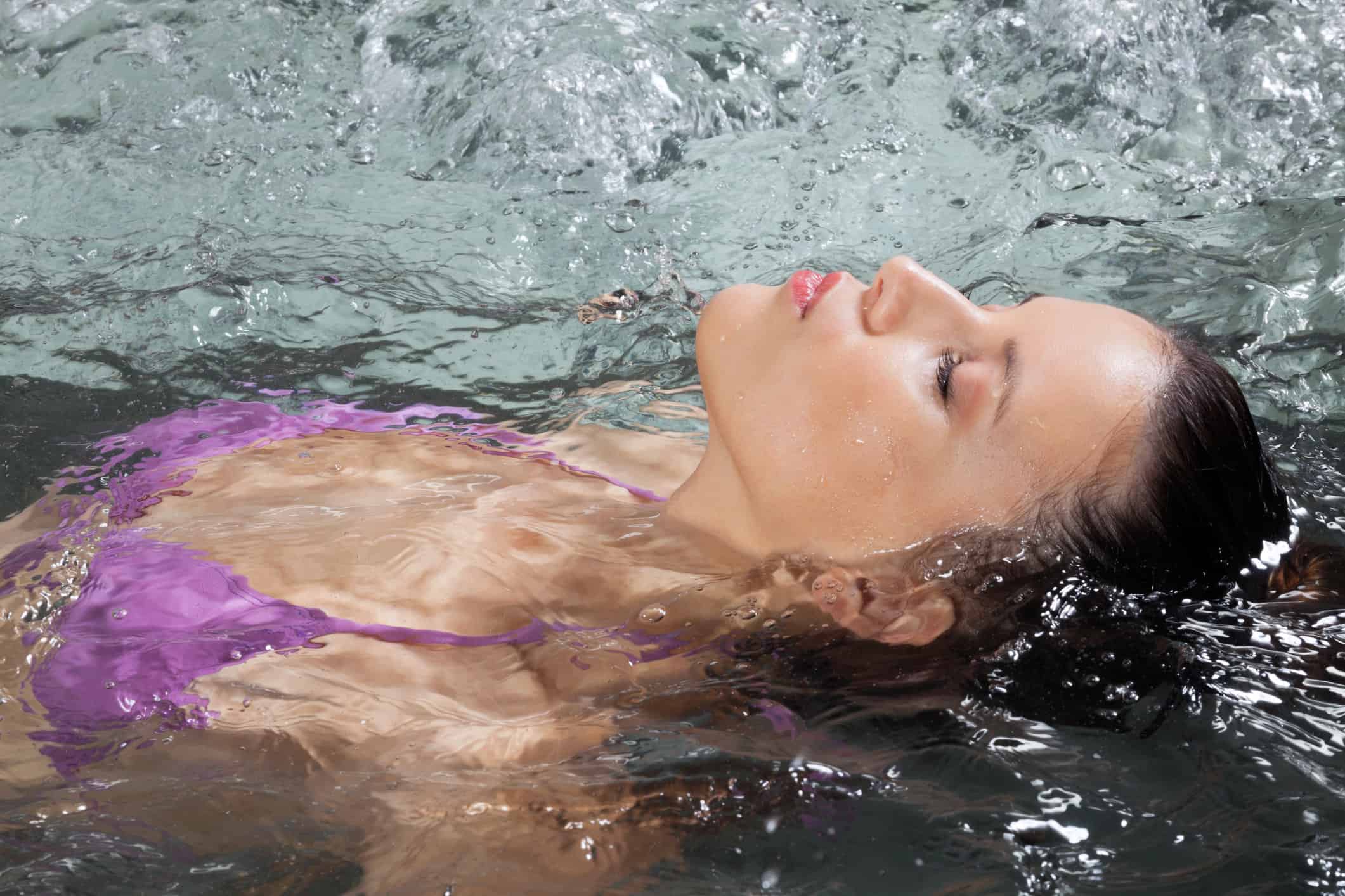 A woman floating in a hot tub with her eyes closed.