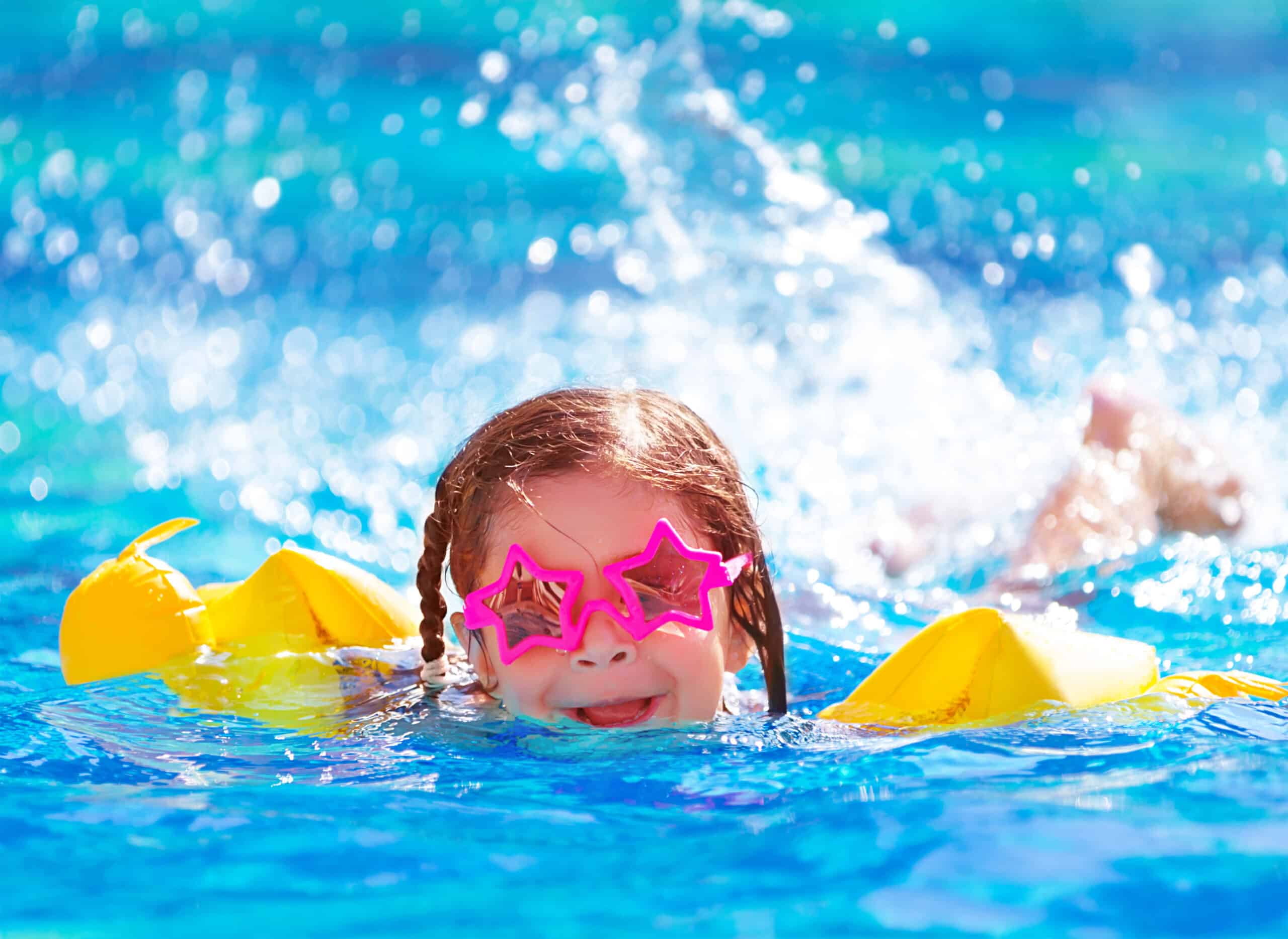 A girl wearing star-shaped glasses and water wings is swimming in a pool.